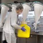 Opérateur manipulant un conteneur avec le système SafeCan devant un isolateur pharmaceutique en zone confinée