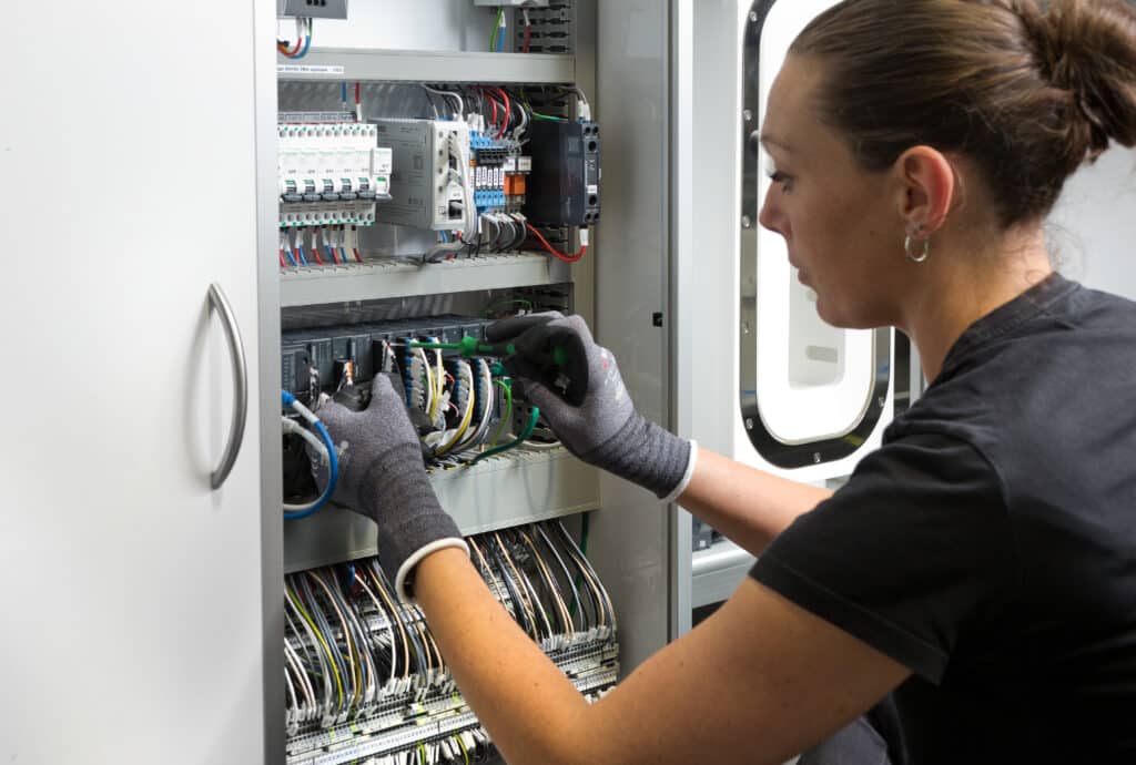 Technicien maintenance JCE Biotechnology intervenant sur une armoire électrique avec câblage et tournevis